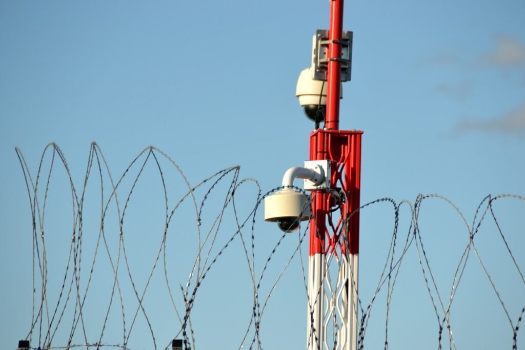 Security cameras on a tower behind barbed wire